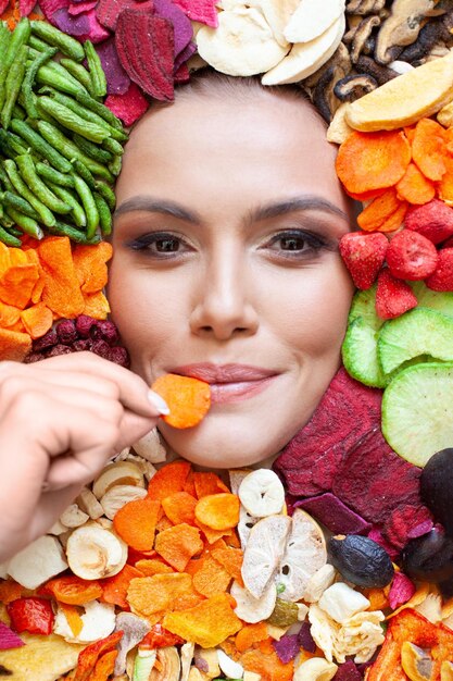 Photo femme heureuse mangeant des carottes chips sur des fruits et légumes chips arrière-plan alimentation saine et concept de régime