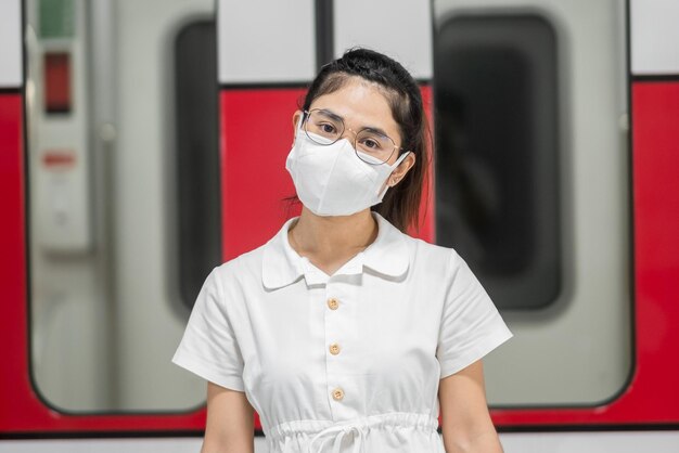 Femme heureuse avec masque de protection contre l'inflexion du coronavirus pendant l'attente du train. transport public. distanciation sociale, nouvelle normalité et sécurité dans le cadre de la pandémie de covid-19