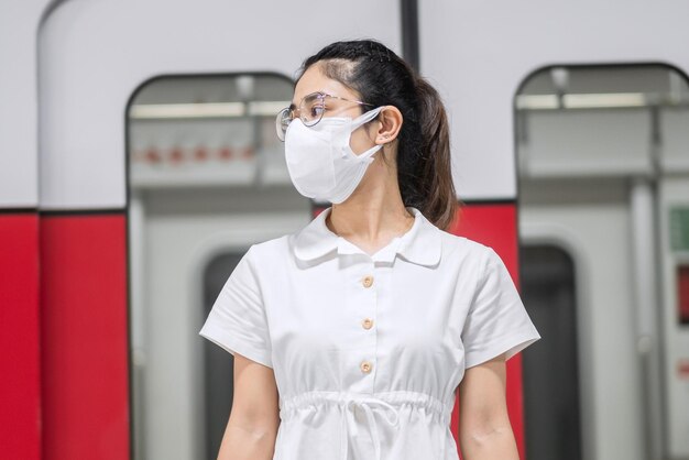 Femme Heureuse Avec Masque De Protection Contre L'inflexion Du Coronavirus Pendant L'attente Du Train. Transport Public. Distanciation Sociale, Nouvelle Normalité Et Sécurité Dans Le Cadre De La Pandémie De Covid-19