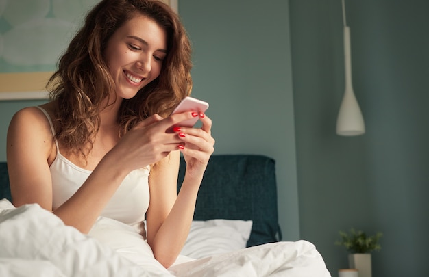 Femme heureuse, messagerie sur smartphone au lit