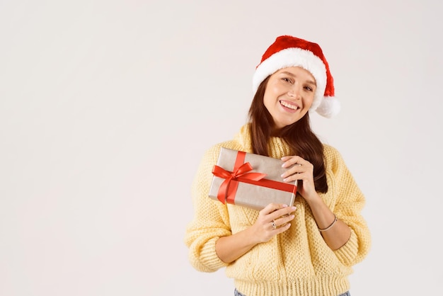 Photo une femme heureuse montrant un cadeau de noël portant un chapeau de père noël rouge isolé sur un fond blanc