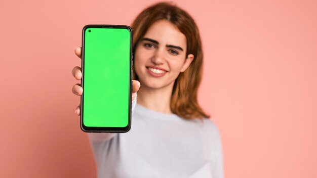 Une femme heureuse montrant un smartphone avec un chromakey en studio