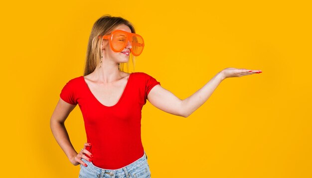 Une femme heureuse montre un espace de copie sur la paume belle fille dans des verres tient quelque chose sur la publicité