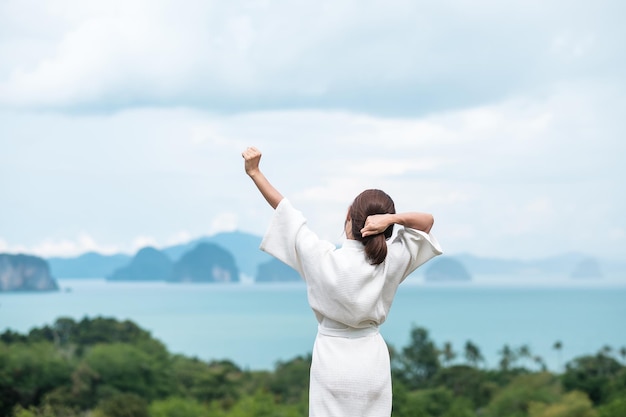 Femme heureuse en peignoir qui s'étend après le réveil et profite de la vue sur l'océan