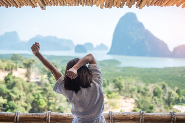 Femme heureuse en peignoir qui s'étire après le réveil et profiter du point de vue de la baie de Phang Nga