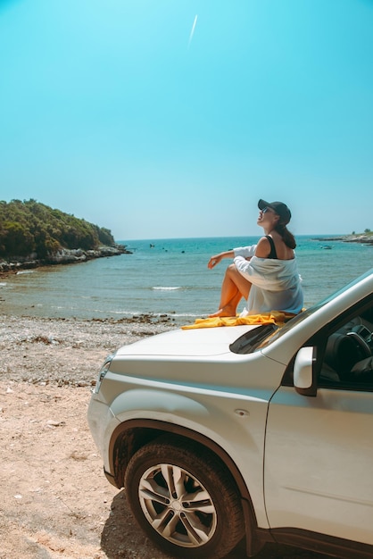 Femme heureuse à la plage d'été de mer se reposant au capot de voiture