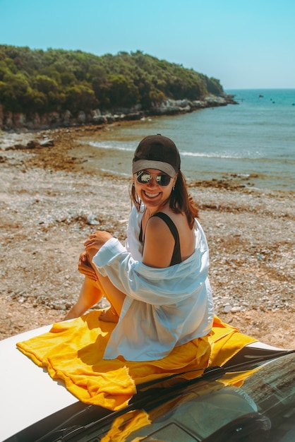 Femme heureuse à la plage d'été de mer se reposant au capot de voiture