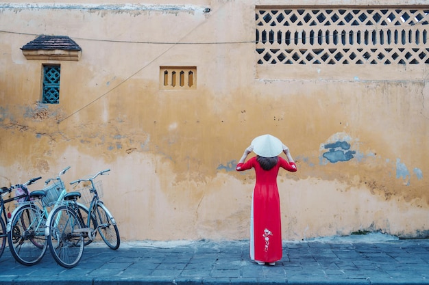 Femme heureuse portant une robe vietnamienne Ao Dai et un chapeau voyageur visitant l'ancienne ville de Hoi An dans le centre du Vietnam et populaire pour les attractions touristiques Concept de voyage au Vietnam et dans le sud-est