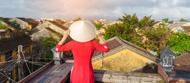 Femme heureuse portant une robe vietnamienne Ao Dai voyageur vue touristique sur le toit de Hoi An, point de repère de la ville ancienne et populaire pour les attractions touristiques Concept de voyage au Vietnam et au sud-est