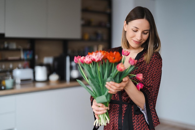 Femme heureuse profitez d'un bouquet de tulipes Femme au foyer bénéficiant d'un bouquet de fleurs et de l'intérieur de la cuisine