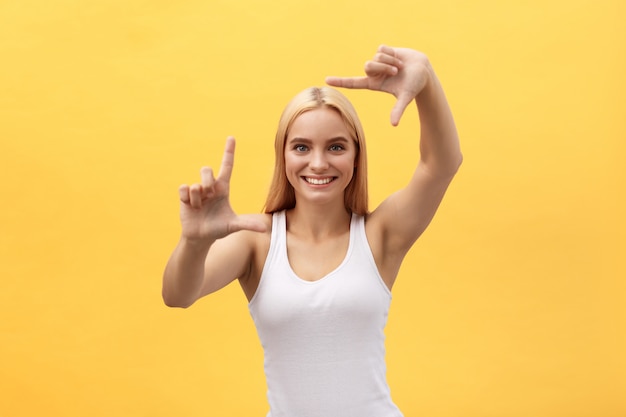 Femme heureuse qui cadre avec les doigts isolés sur un fond jaune.