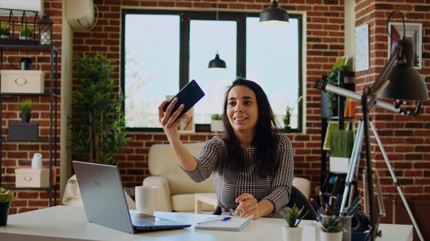 Une femme heureuse qui rit en se faisant un selfie avec son téléphone portable tout en souriant à la maison.