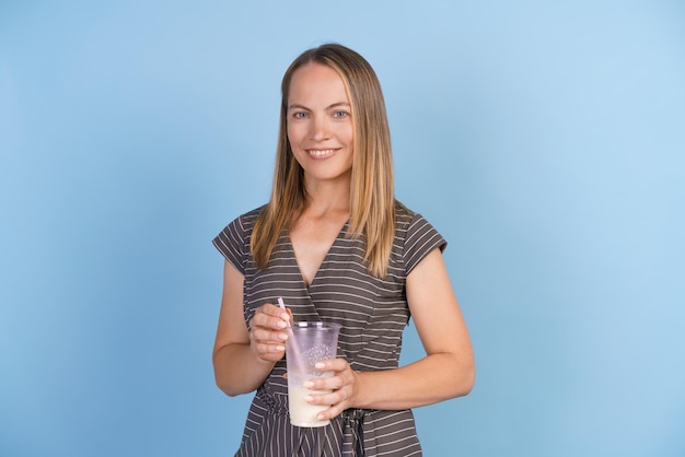 Une femme heureuse en robe grise se tient avec un milk-shake dans les mains et sourit