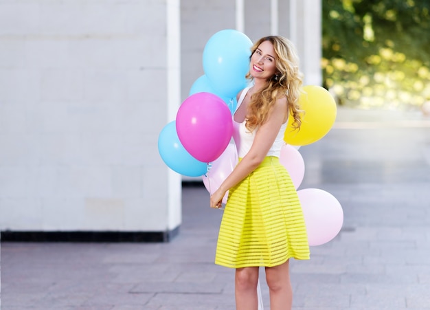 Femme heureuse en robe jaune avec des ballons colorés