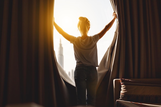 Une femme heureuse s'étire et ouvre les rideaux à la fenêtre le matin