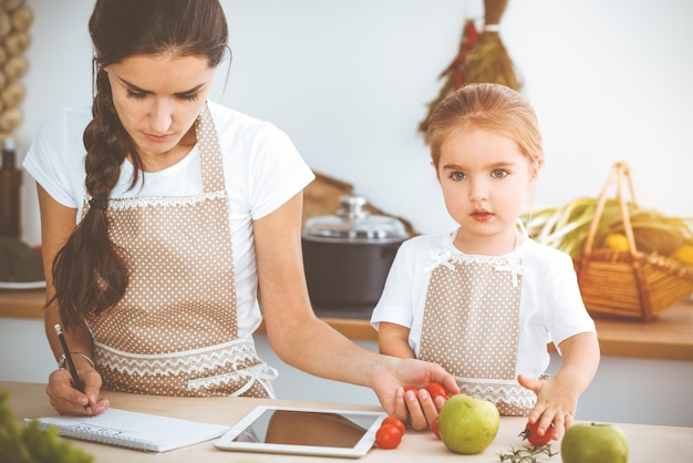 Une femme heureuse et sa fille recherchent de nouvelles recettes pour une cuisine ensoleillée en famille