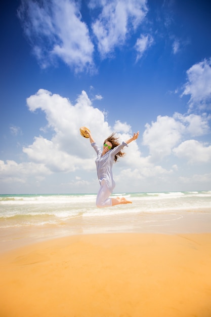 Femme heureuse sautant à la plage contre le ciel bleu Concept de vacances d'été