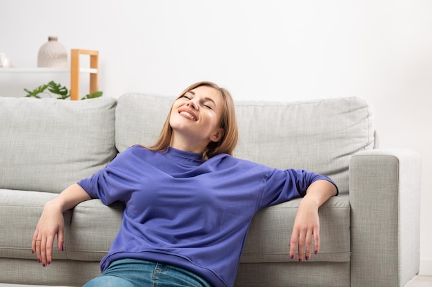 Une femme heureuse se détend sur le canapé en respirant l'air frais du climatiseur en profitant du climat confortable dans le salon ventilé en méditant les yeux fermés Confort à la maison