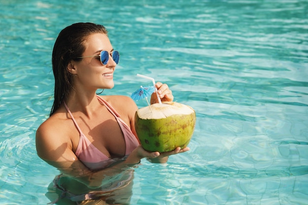 Femme heureuse se détendre dans la piscine et boire de l'eau de coco