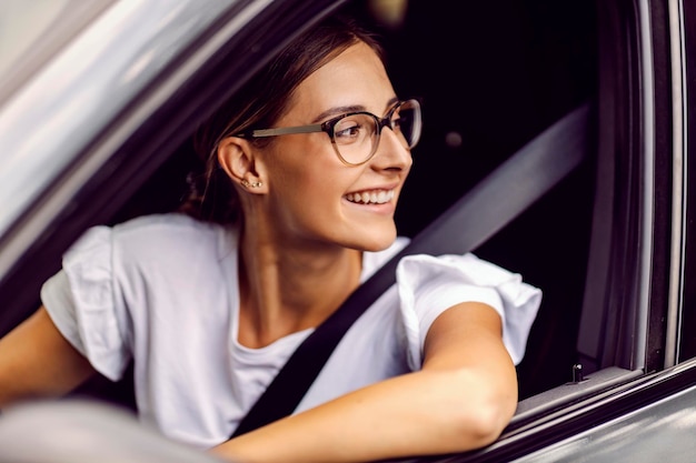 Une femme heureuse se penche sur la fenêtre de la voiture et regarde à travers pendant la conduite