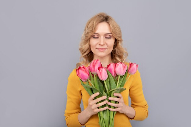 Une femme heureuse sent les tulipes sur fond gris