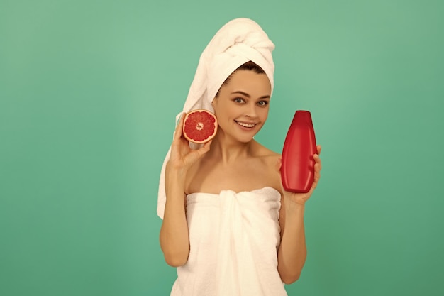 Femme heureuse en serviette avec une bouteille de shampoing au pamplemousse sur fond bleu