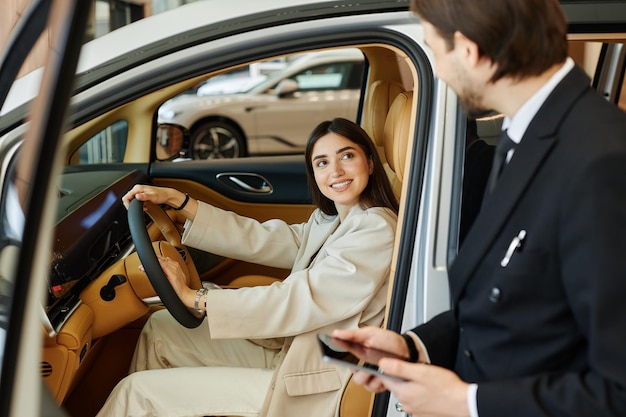 Femme heureuse sur le siège du conducteur testant une démo de voiture au centre de concessionnaires