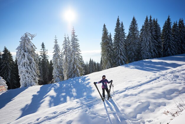 Femme heureuse avec ski debout au milieu de la pente de la montagne couverte de neige