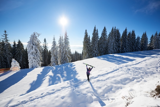 Femme heureuse avec des skis debout au milieu de la pente de la montagne couverte de neige. Journée ensoleillée pendant les vacances d'hiver. Vue générale.
