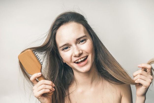 Une femme heureuse sourit avec un peigne à cheveux à la main, soins capillaires de beauté