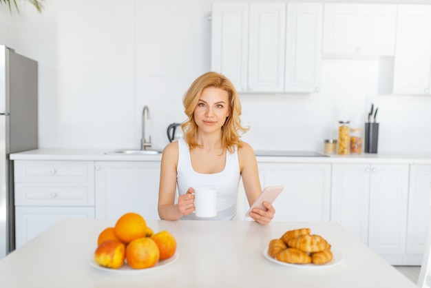 Femme heureuse à la table avec des fruits et de la pâtisserie