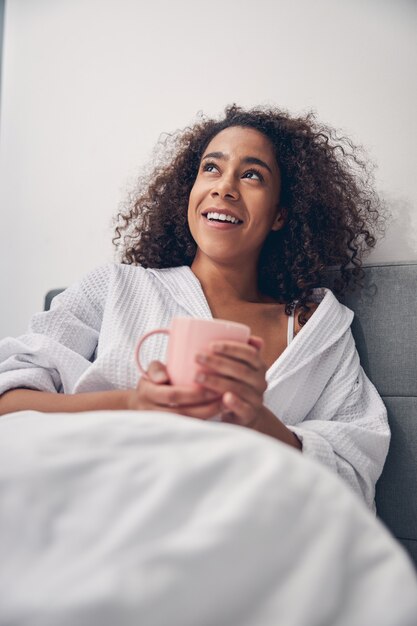 Photo femme heureuse avec une tasse de thé à la camomille assise dans son lit