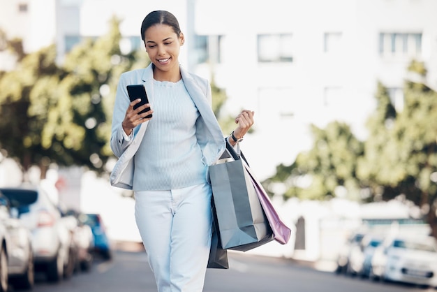 Femme heureuse téléphone et sac d'achat en ville pour la communication sur les médias sociaux ou le réseautage en plein air Personne féminine ou acheteur sur une application de smartphone mobile pour le chat en ligne en marchant dans la rue d'une ville urbaine