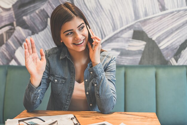 La femme heureuse téléphone à la table dans un café