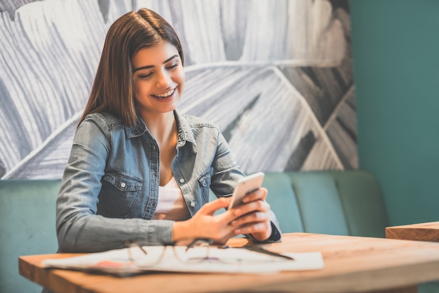 La femme heureuse téléphone à la table dans un café