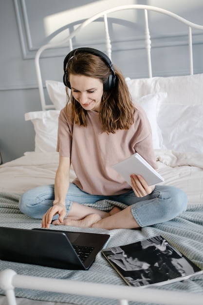 Femme heureuse en tenue décontractée avec les écouteurs travaillant sur un ordinateur portable à distance de la maison