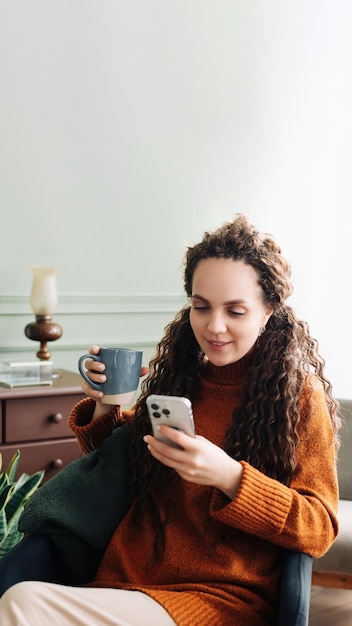 Femme heureuse utilisant un smartphone et buvant du café à la maison dame souriante avec téléphone et café appréciant