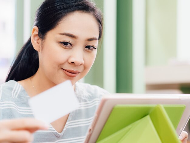 Femme heureuse utilise une carte de crédit maquette blanche pour faire des achats en ligne sur tablette.