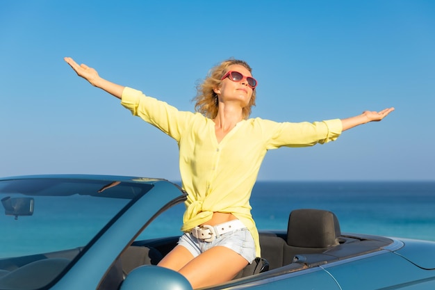Femme heureuse voyageant en voiture à la mer Personne s'amusant en cabriolet bleu Concept de vacances d'été
