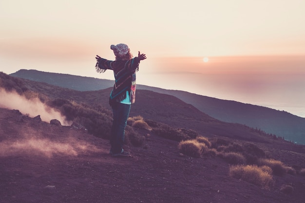 Femme heureuse de voyageur vue de l'arrière ouvrant les bras pour embrasser la merveilleuse nature impressionnante pendant l'heure du coucher du soleil