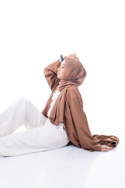 Une femme en hijab est assise sur le sol sur fond blanc.