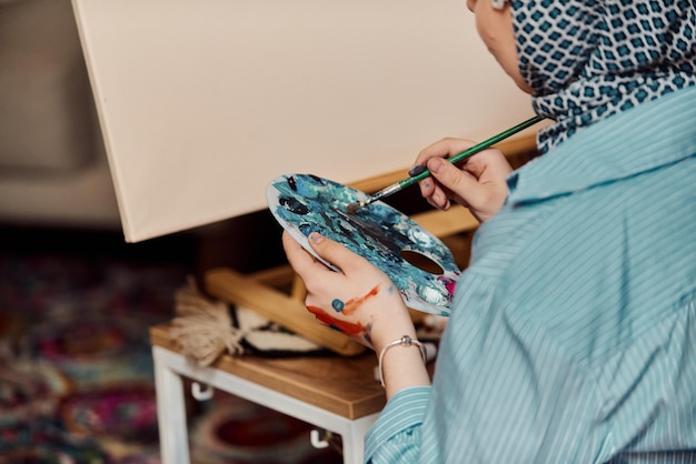 Une femme en hijab peint sur toile avec un pinceau et une détrempe