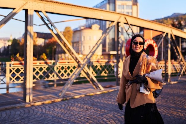 Une femme hijab portant des lunettes de soleil élégantes et une élégante tenue française se promenant dans la ville au coucher du soleil