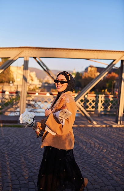 Une femme hijab portant des lunettes de soleil élégantes et une élégante tenue française se promenant dans la ville au coucher du soleil