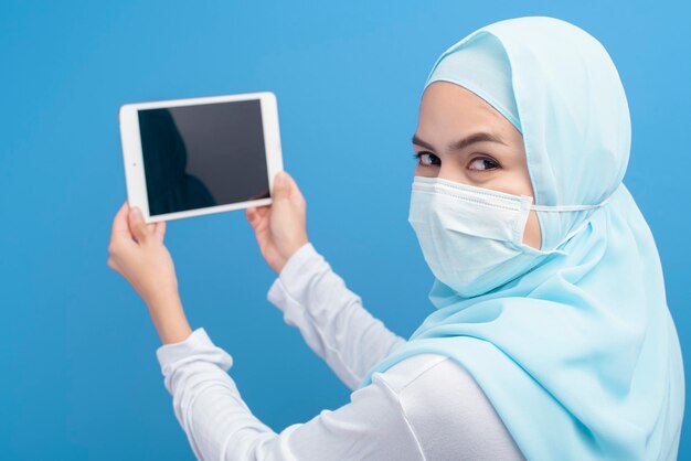 Femme avec hijab portant un masque chirurgical à l'aide de tablette