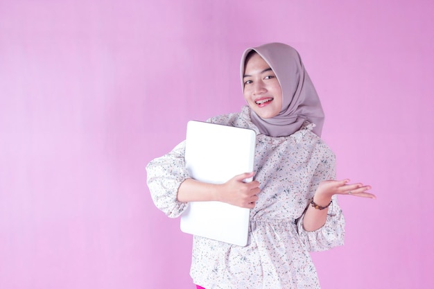 Une femme en hijab tient un cahier et sourit.