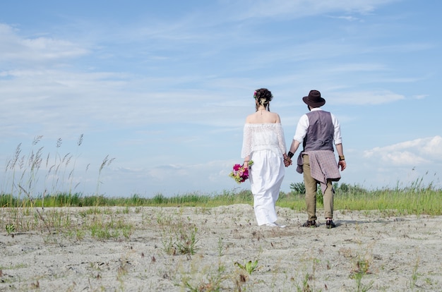 Femme hippie élégante en robe ethnique blanche, main dans la main avec l'homme