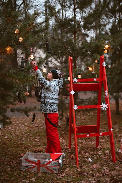 Une femme hipster décore des arbres de Noël avant que l'escabeau rouge ne s'élève pour célébrer le nouvel an 2022 à l'extérieur pour une fête, Préparation pour la célébration bonne année