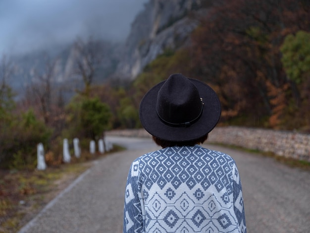 Femme hipster élégante dans un chapeau marchant sur une route de montagne