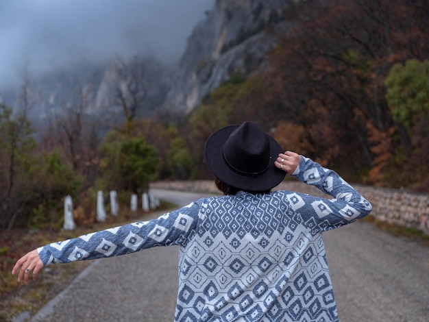 Femme hipster élégante dans un chapeau marchant sur une route de montagne